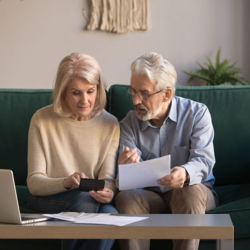 Serious mature couple calculating bills to pay, checking domestic finances, middle aged family managing, planning budget, expenses, grey haired man and woman reading bank loan documents at home